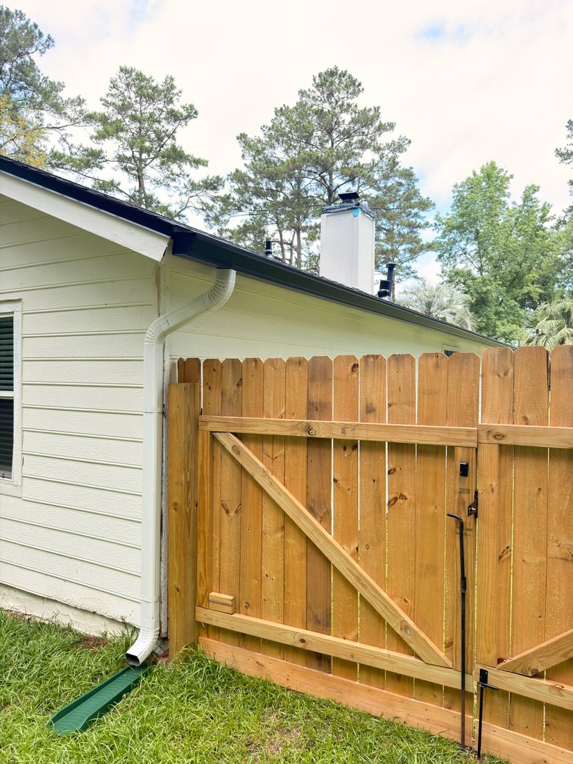 White home corner with a seamless gutter and downspout beside a wood privacy fence
