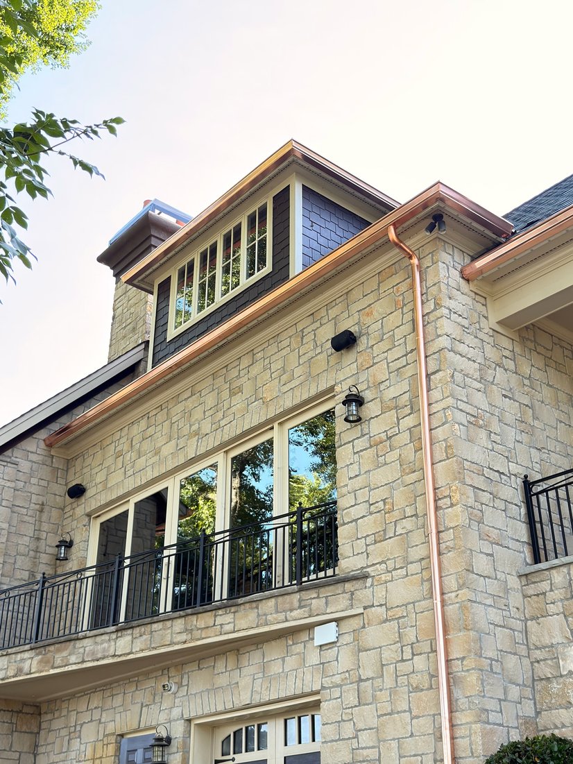 Stone home with copper seamless gutters and a downspout
