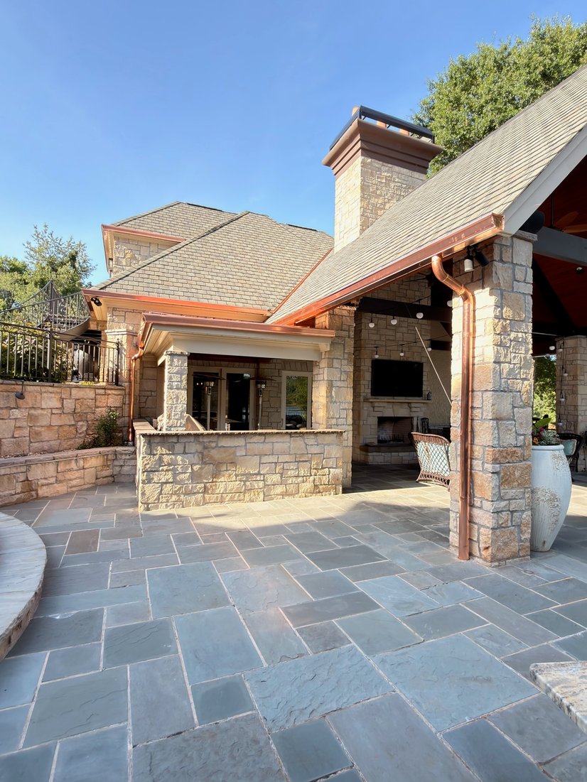 Stone home with copper seamless gutters and downspouts over a flagstone patio