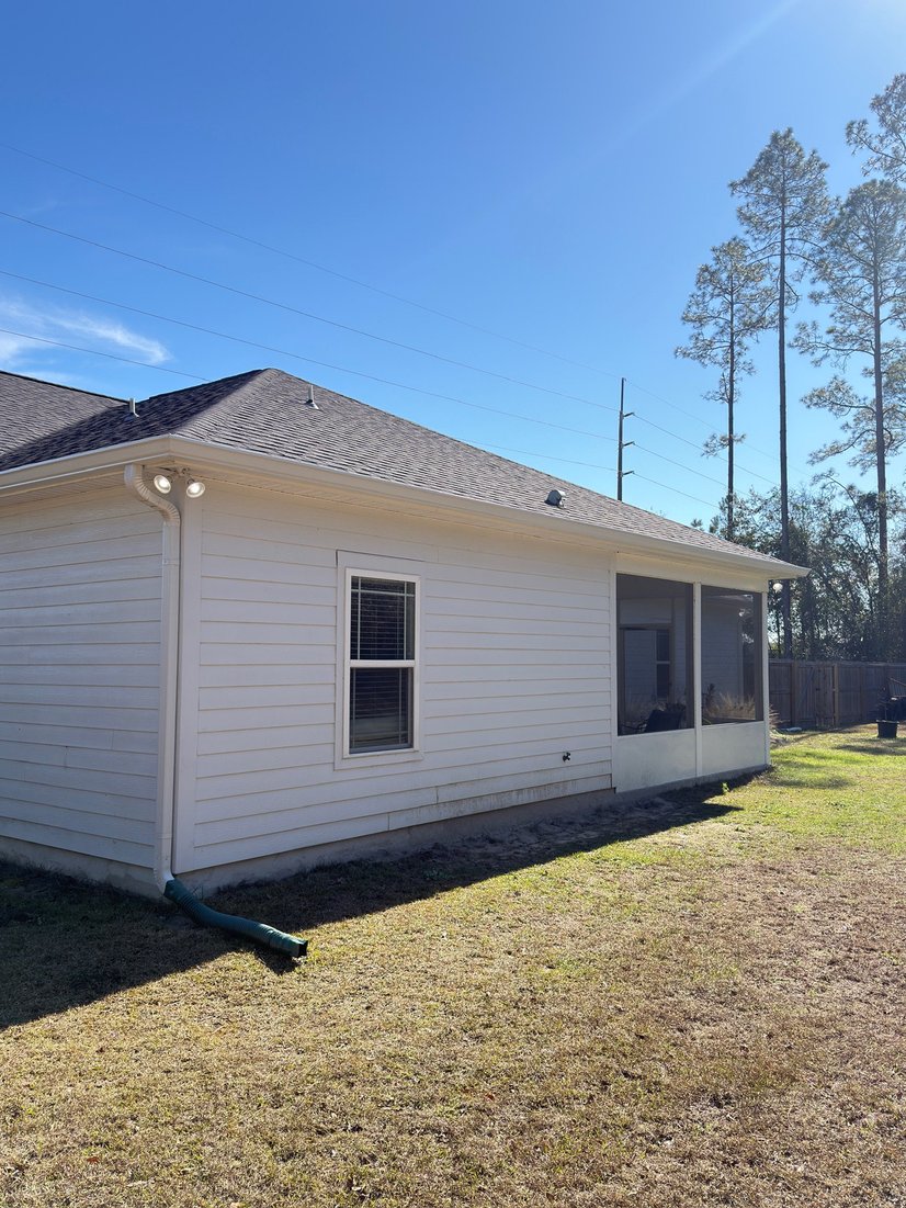 White home corner with a seamless gutter and downspout draining to the yard