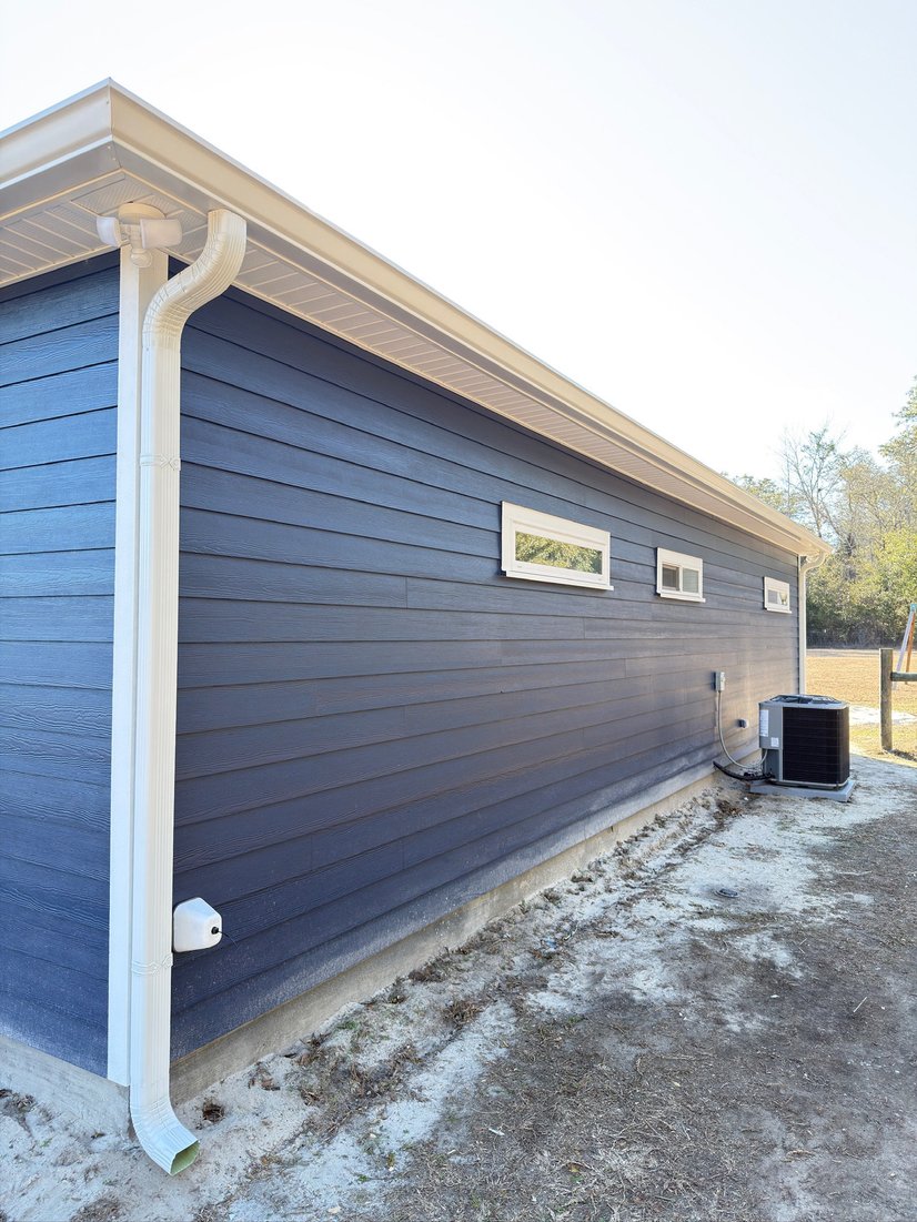Navy blue home side wall with a white seamless gutter and downspout