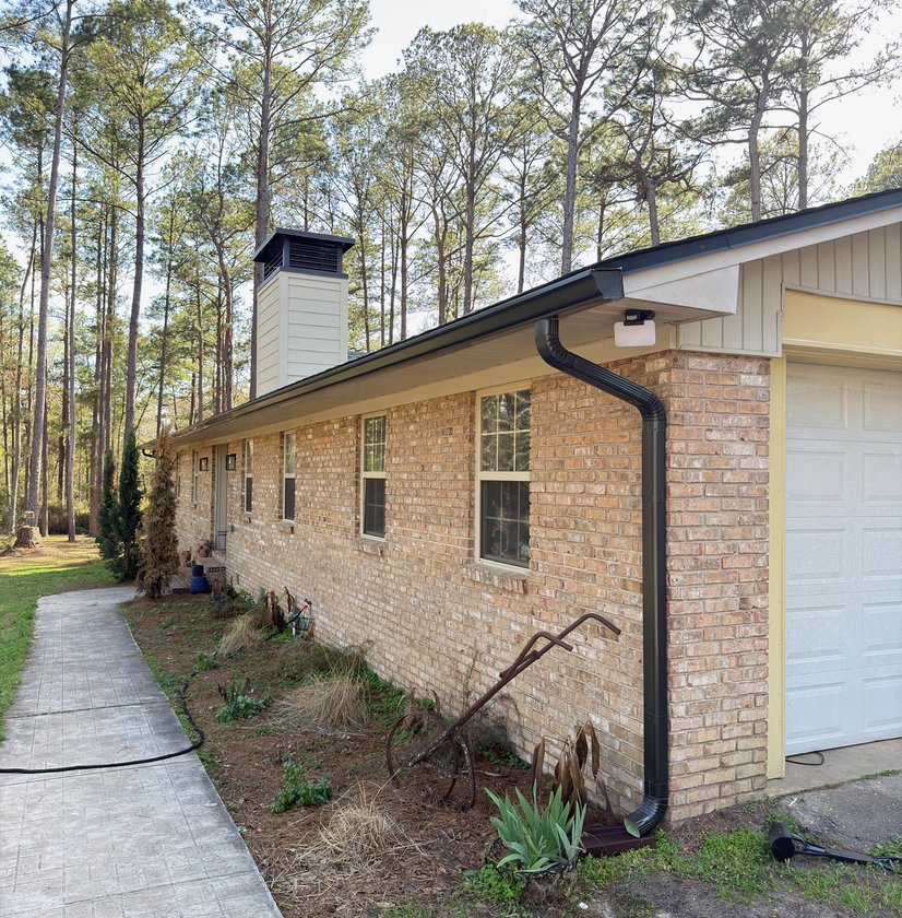 Black seamless gutter and downspout installed on a brick ranch home